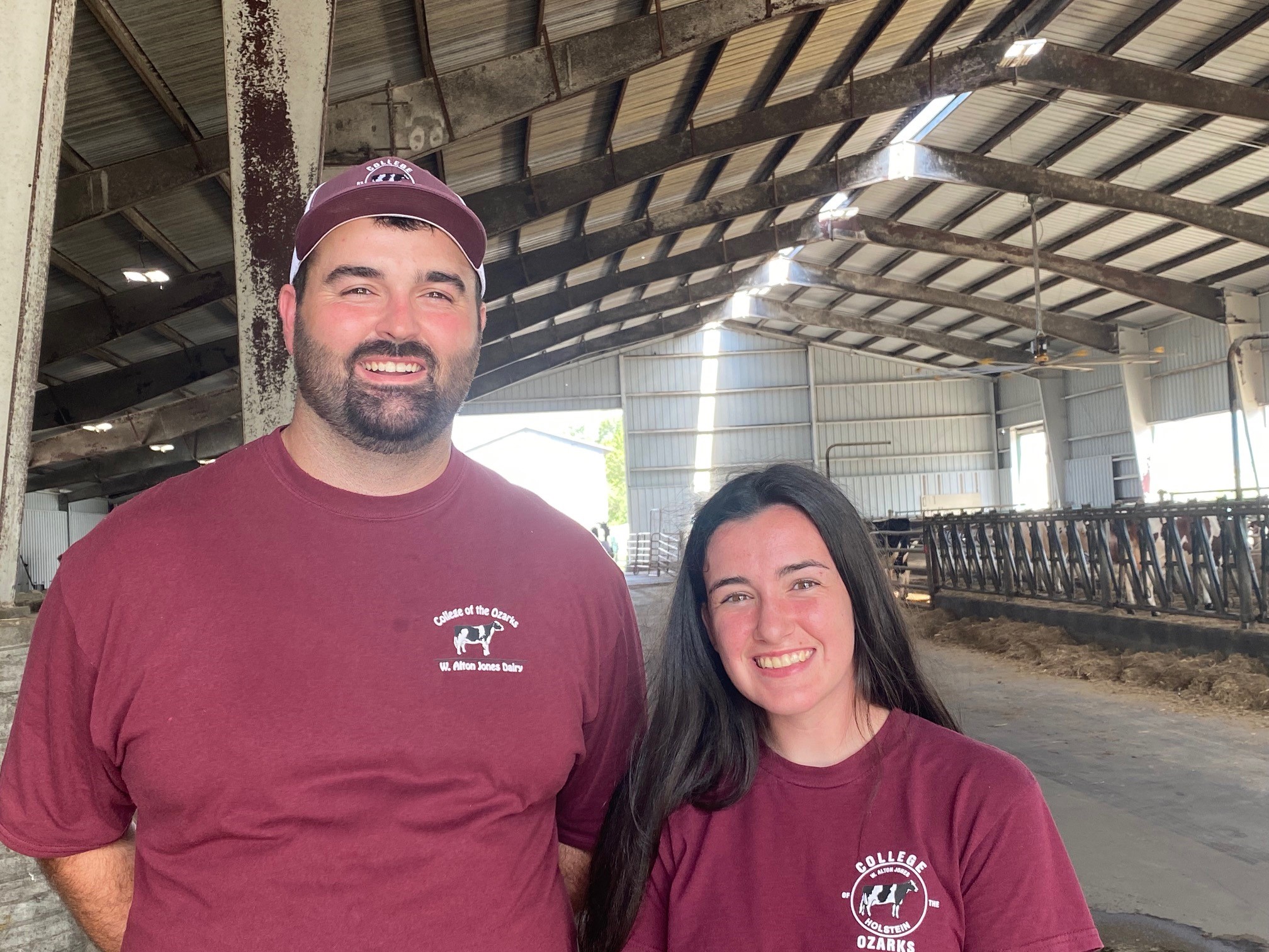 A man and woman in maroon shirts stand in a barn