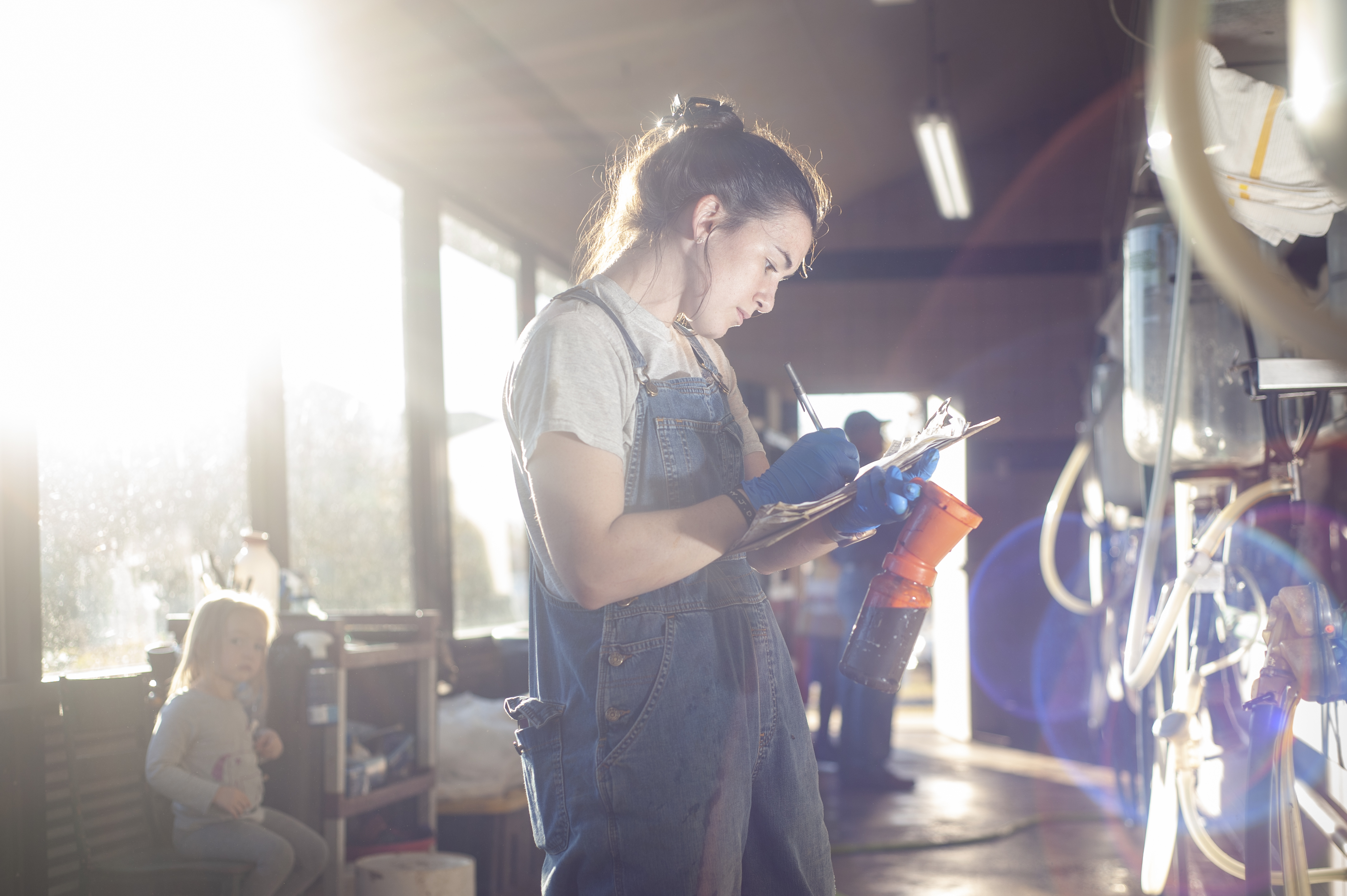 a woman stands with a clipboard by milking machinery
